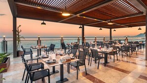 A restaurant with outdoor seating, tables set with dinnerware, and a view of the sea. - DOBEDAN WORLD PALACE - All inclusive (Kemer)