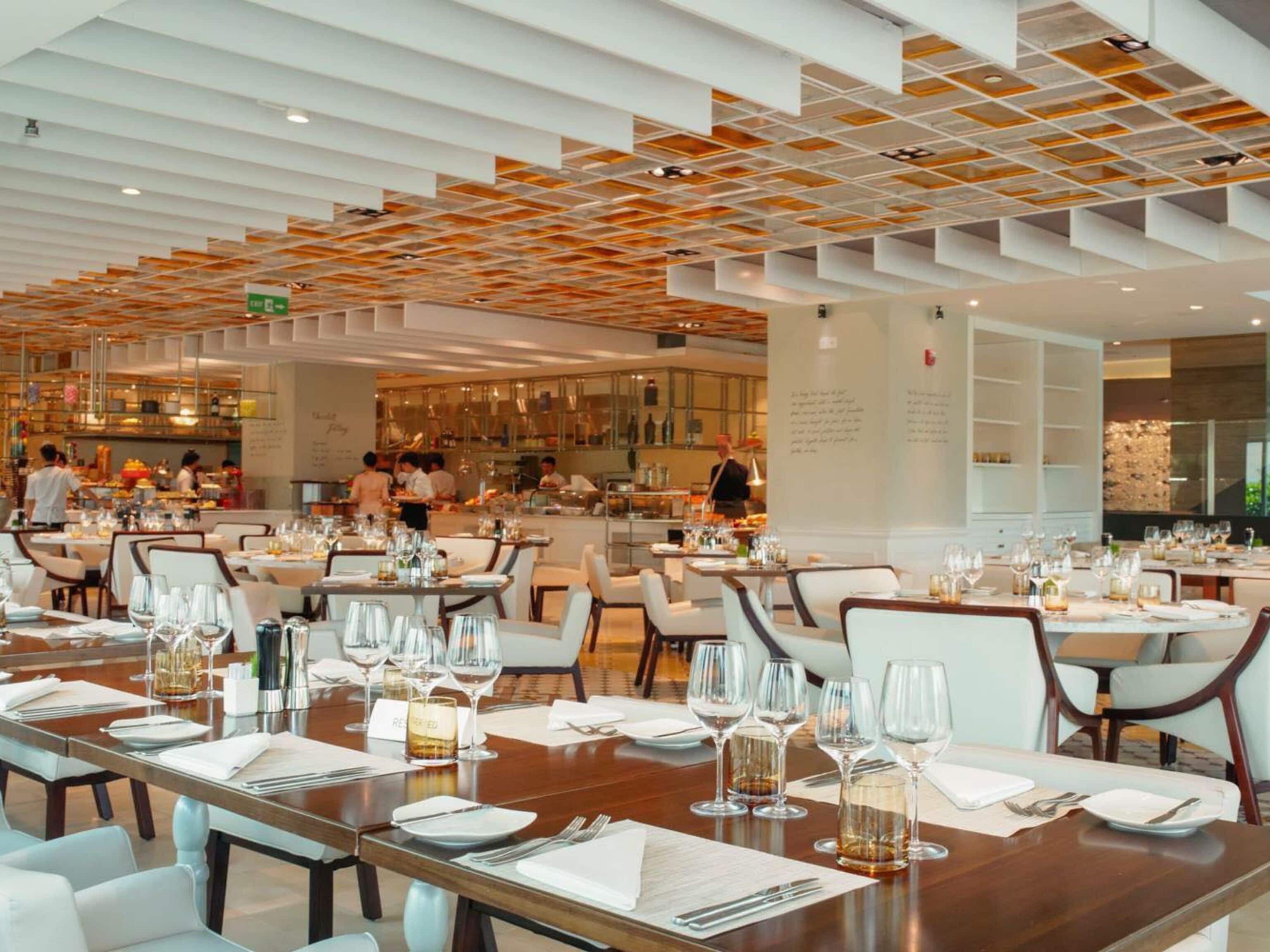 A modern restaurant with multiple dining tables, each set with wine glasses, plates, and cutlery.