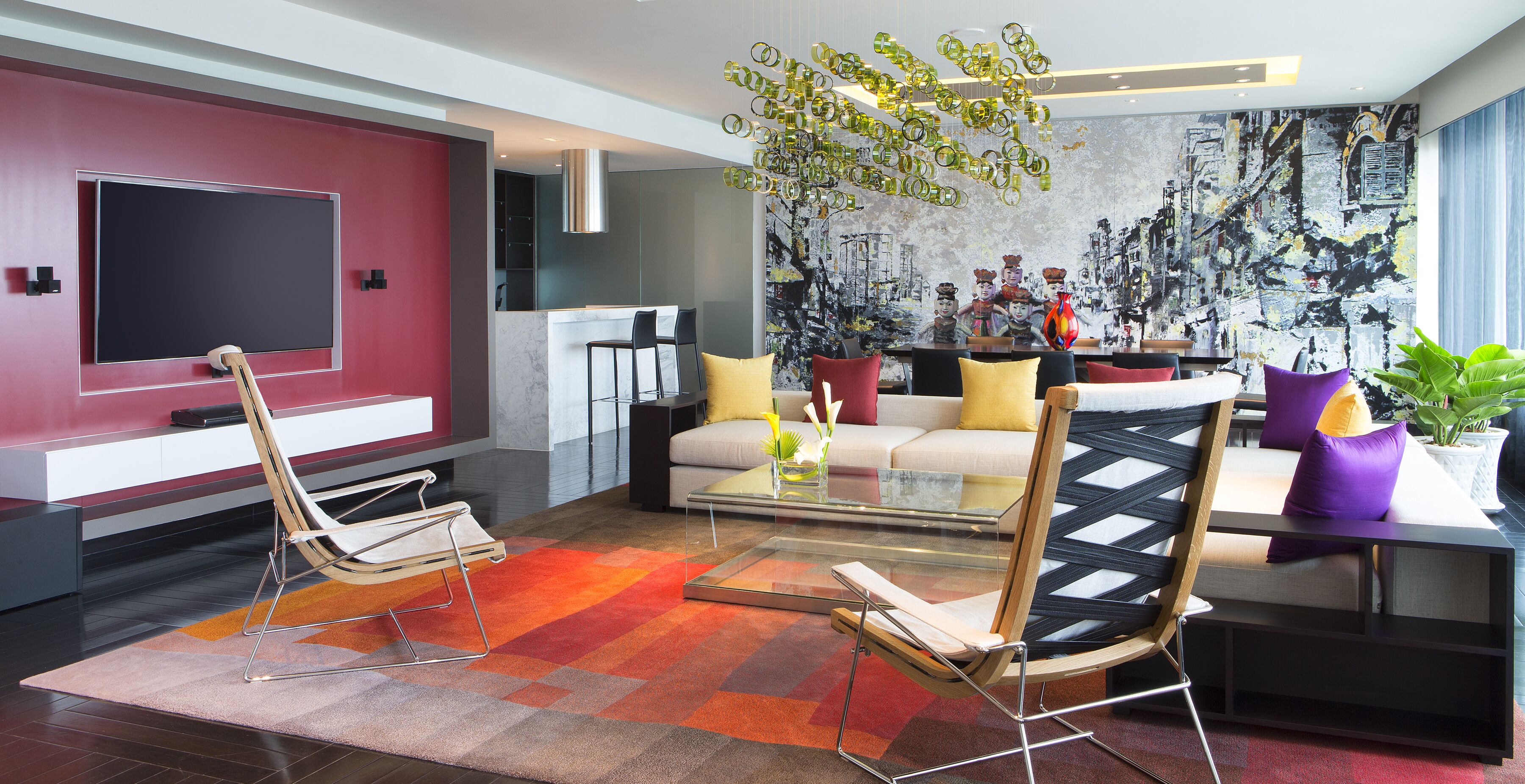 Een moderne woonkamer met een grote flatscreen televisie, een bank, twee fauteuils, een salontafel en een kleurrijk vloerkleed.