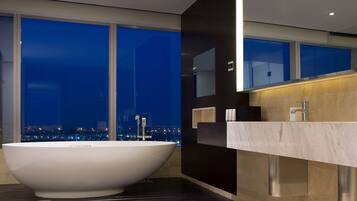 Een moderne badkamer met een vrijstaand bad, een grote spiegel en uitzicht op een stadsbeeld in de nacht.