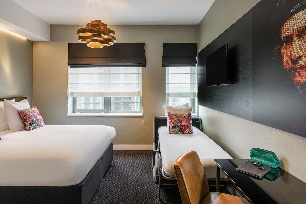 A hotel room with two beds, a desk, a chair, a TV, and a window with blinds.