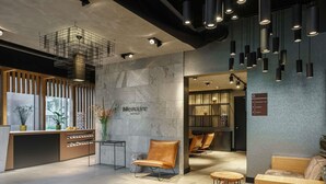 Un hall d’hôtel moderne comprenant un comptoir d’accueil, un espace salon et un panneau indiquant l’emplacement du restaurant, de l’ascenseur et des toilettes.