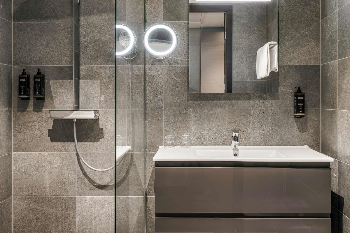 Une salle de bain moderne avec une douche à parois de verre, un meuble-lavabo avec un miroir et deux appliques murales éclairées.