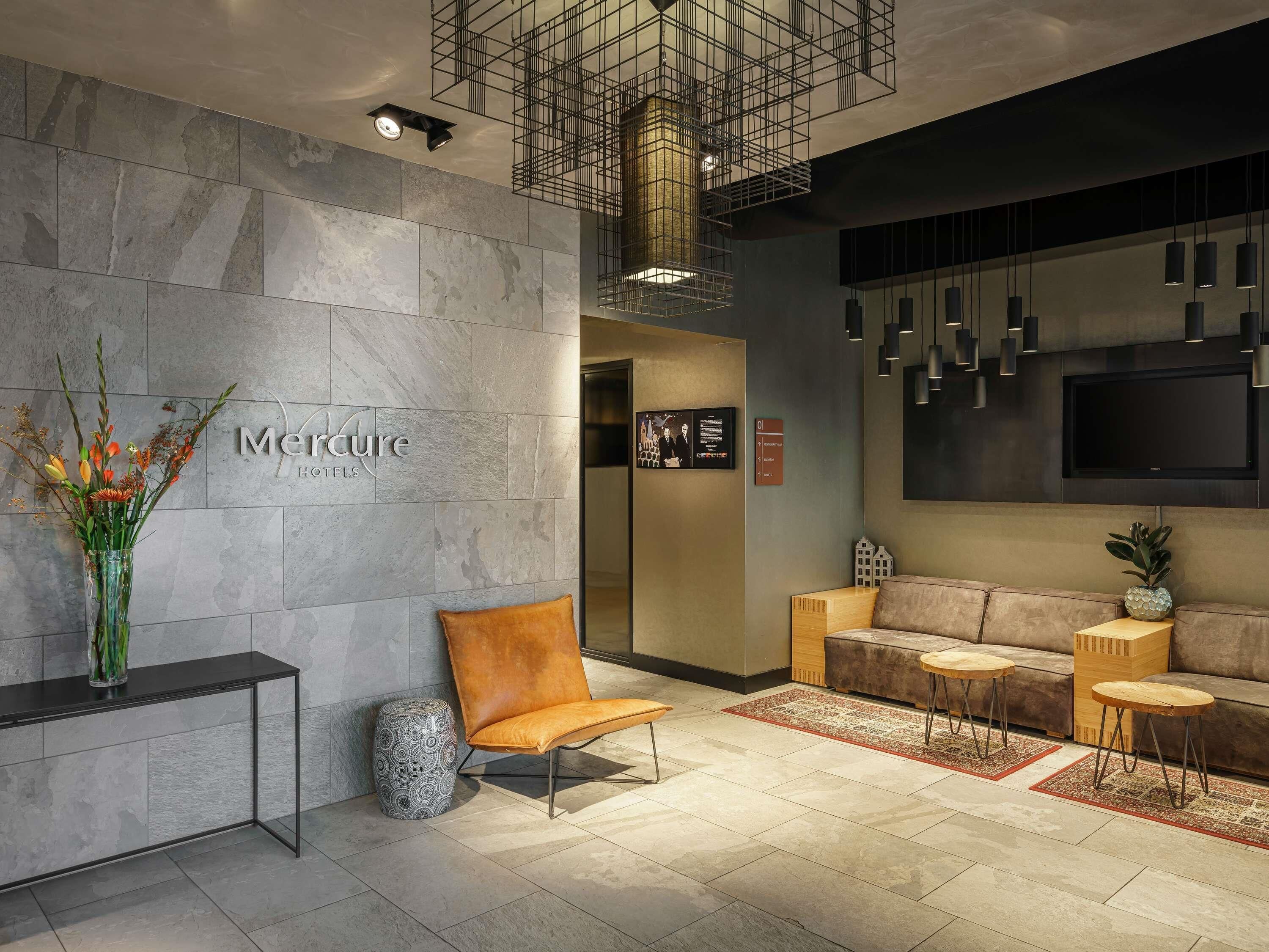 A modern hotel lobby with a reception desk, seating area, and a television screen.