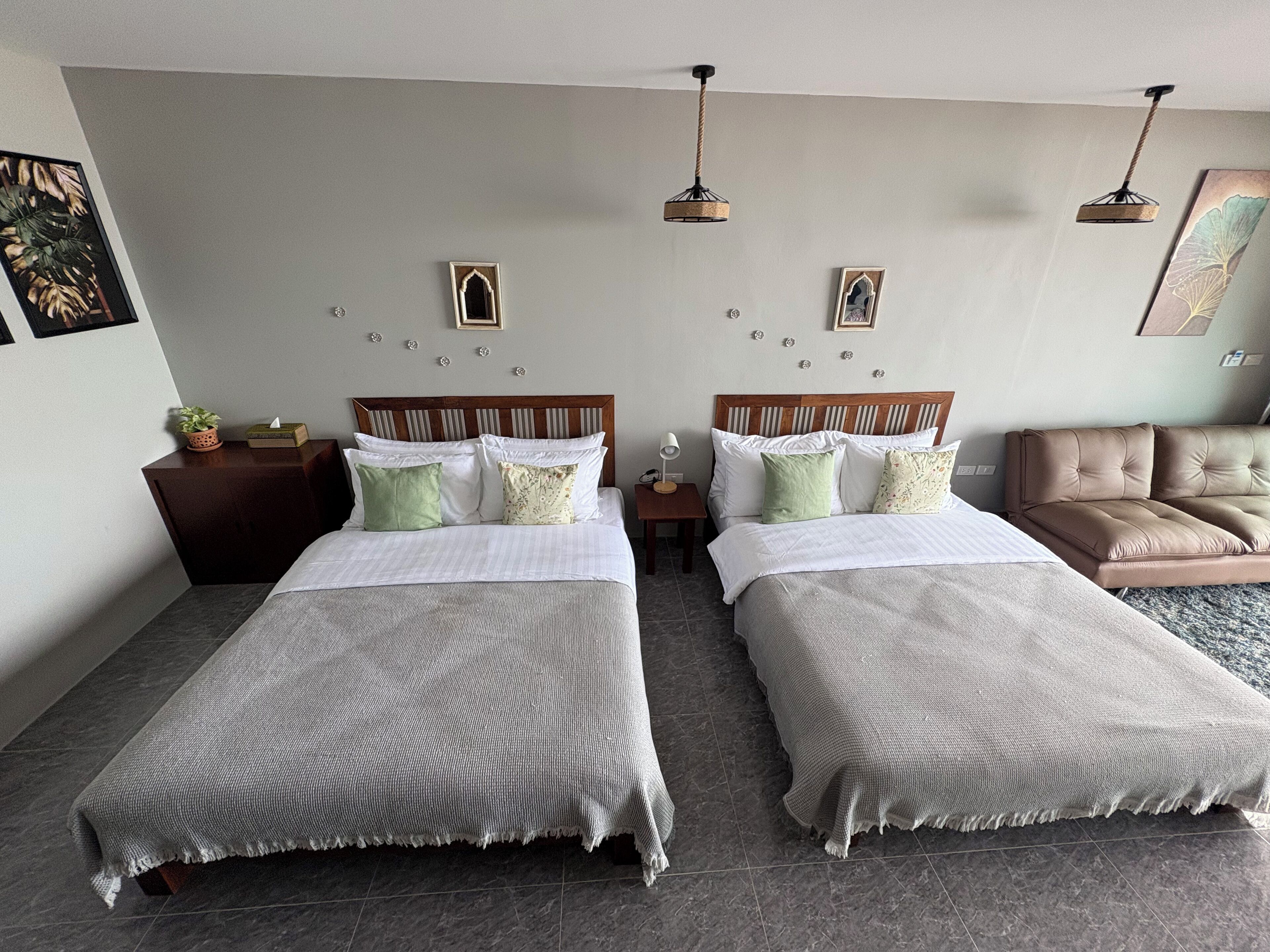 A hotel room with two beds, a sofa, a nightstand, and decorative wall art.
