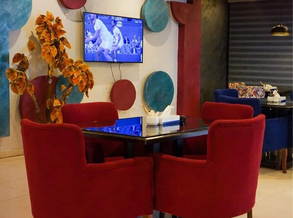A dining area with red chairs, a glass table, and a TV mounted on the wall displaying a sports event.