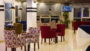 Un vestíbulo de hotel con una mezcla de sillas estampadas y de color liso, una pantalla grande y una planta.