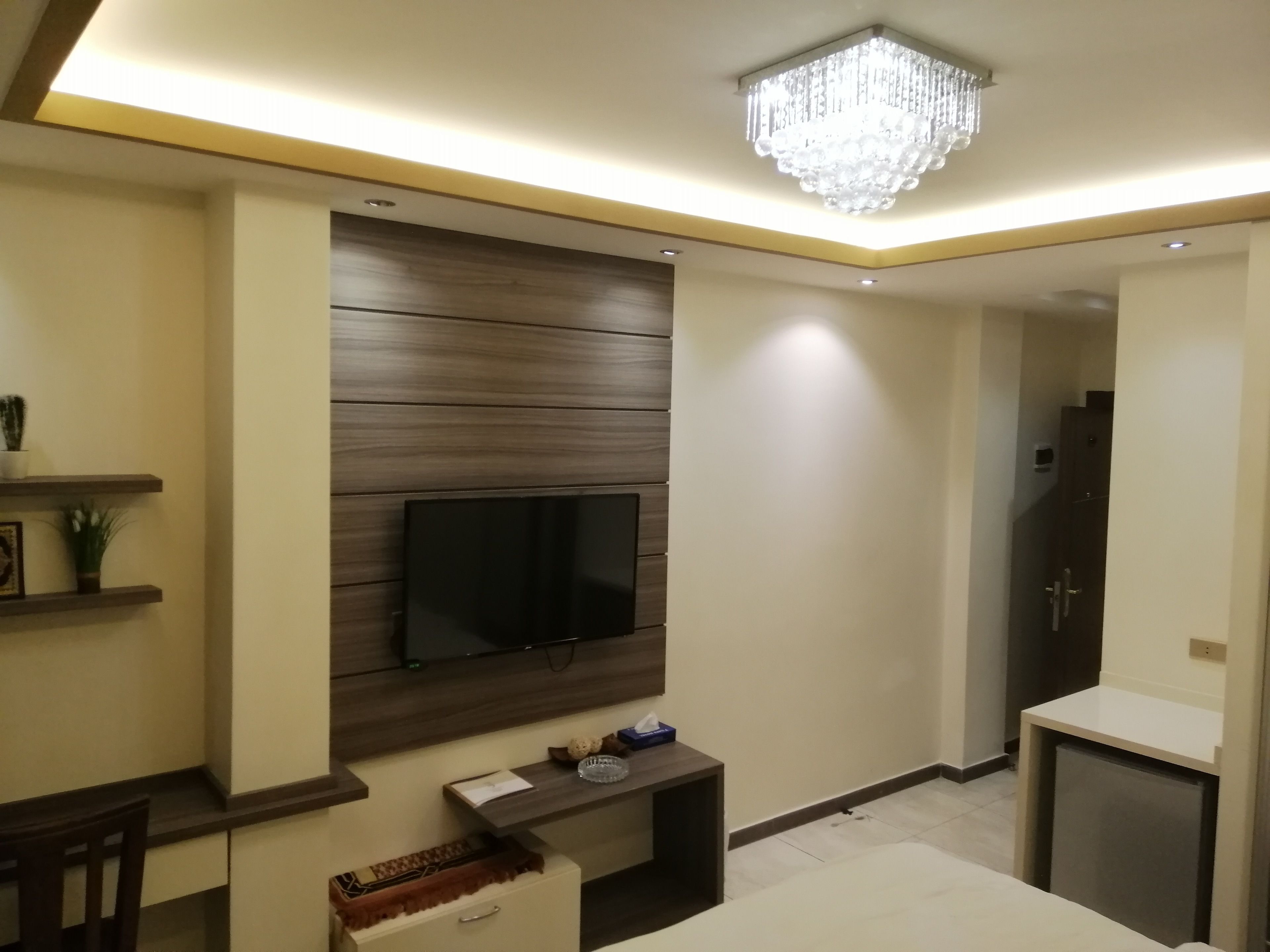 A modern living room with a flat-screen TV mounted on a wooden panel wall, a small side table with a tissue box, and a decorative item.
