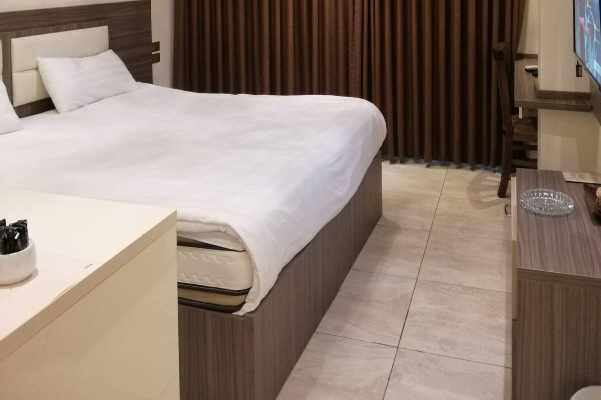 Habitació d'hotel amb un llit gran, una taula de nit, un televisor i una cortina.