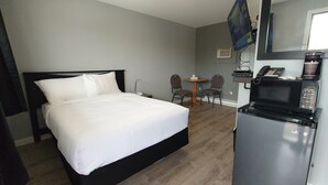 Habitación de hotel con cama, escritorio con computadora, microondas y televisor montado en la pared.