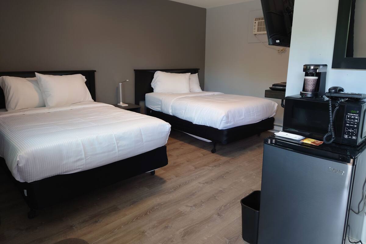 A hotel room with two beds, a coffee machine, a TV, and a trash bin.