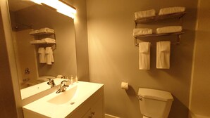 Un baño con lavamanos, espejo y retrete. Hay toallas colgadas en un perchero sobre el retrete.