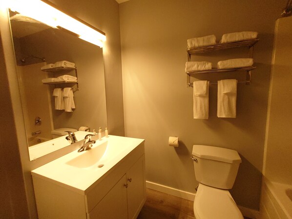 Une salle de bain avec un lavabo, un miroir et des toilettes. Des serviettes sont suspendues sur un porte-serviettes au-dessus des toilettes.