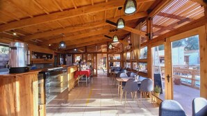 A wooden interior with a bar area, tables, and chairs, and large windows allowing natural light.