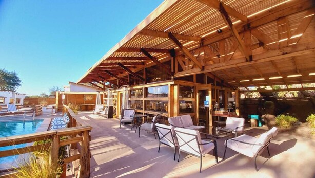 An outdoor patio area with a pool, wooden pergola, and seating arrangements.