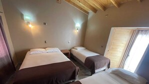 A room with two beds, each with a wooden headboard, and a window with a view of the outside.