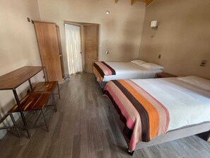 A small, compact room with two single beds, a wooden desk, and a wardrobe.