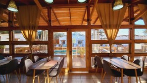 A restaurant with wooden tables and chairs, large windows, and a view of a pool area.