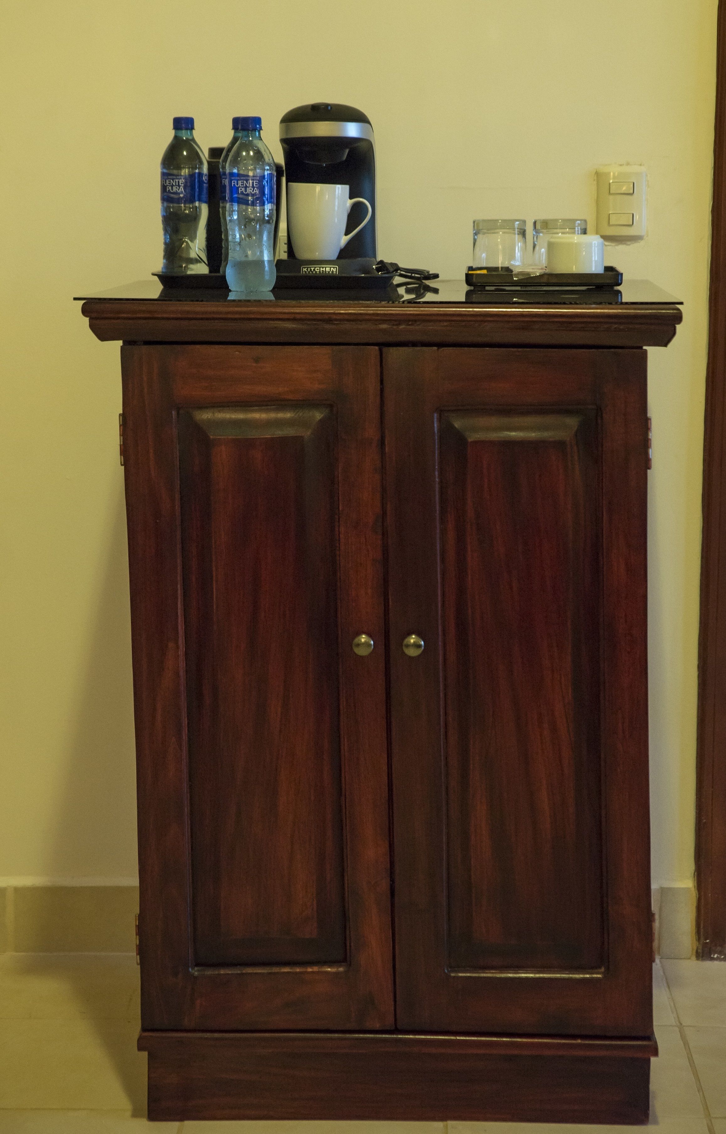 A wooden cabinet with two doors, a coffee maker, and two water bottles on top.