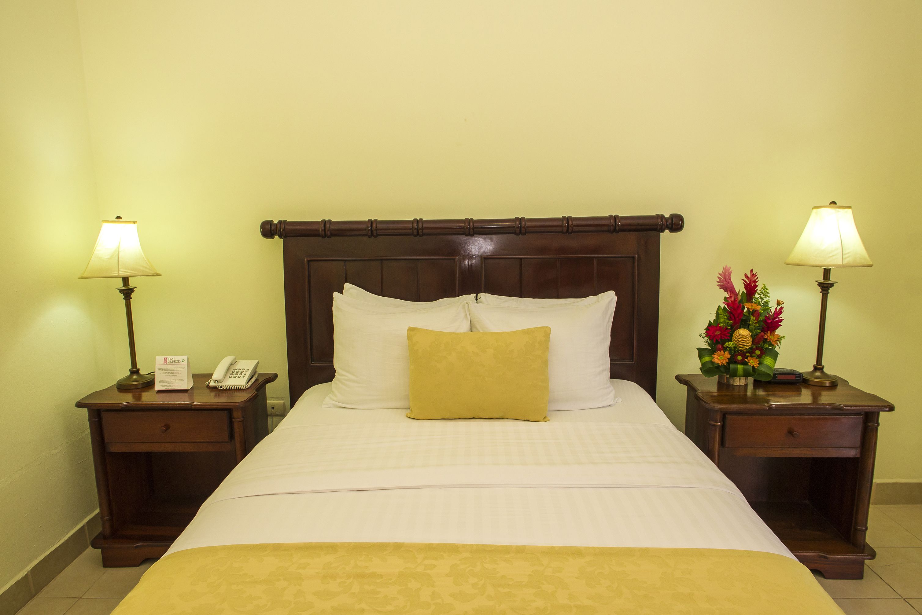A hotel room with a large bed, two bedside tables with lamps, a telephone, and a floral arrangement.