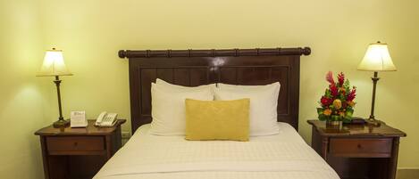A hotel room with a large bed, two bedside tables with lamps, a telephone, and a floral arrangement.