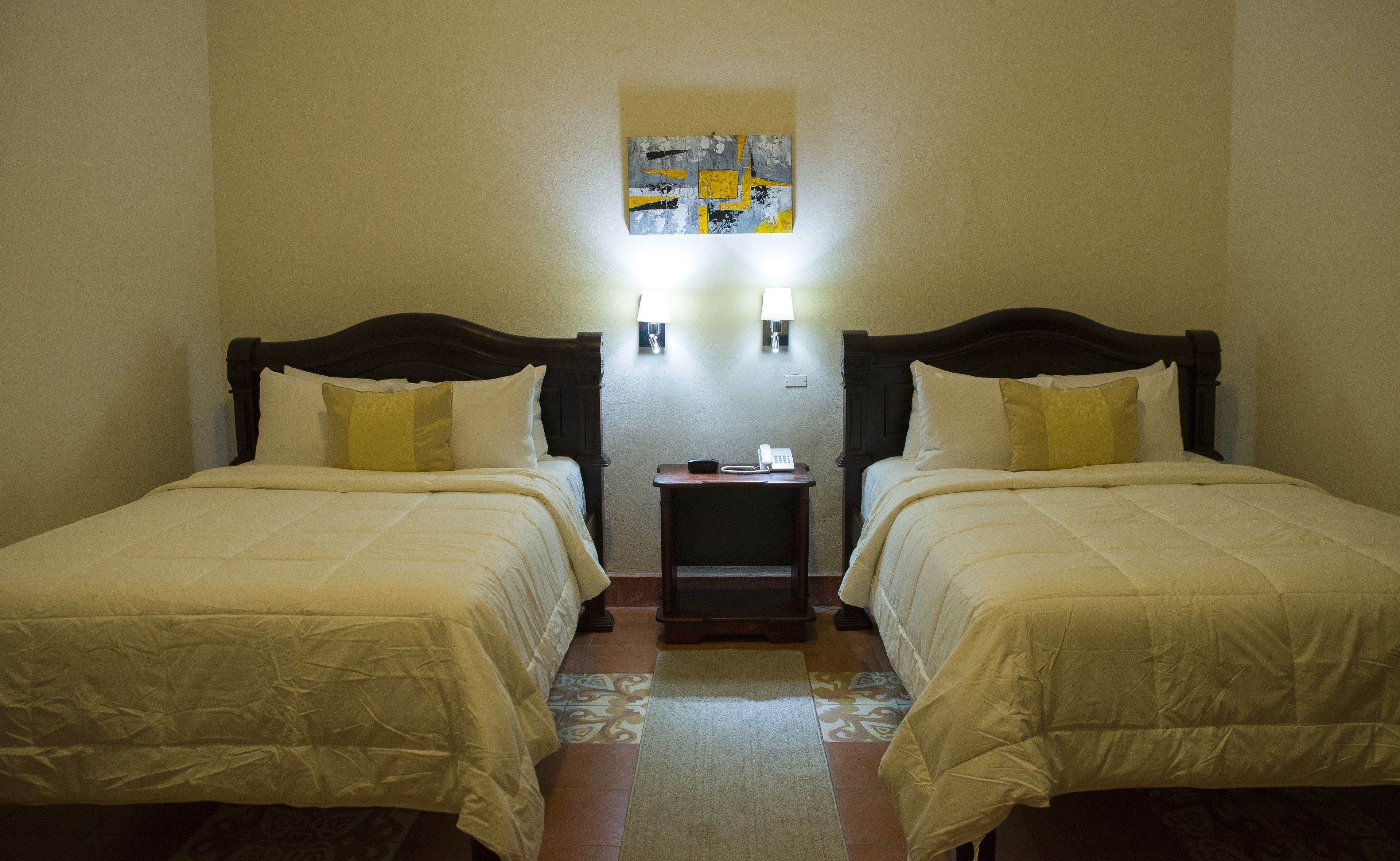 Habitación de hotel con dos camas individuales, una mesita de noche pequeña con un teléfono y dos lámparas de pared.