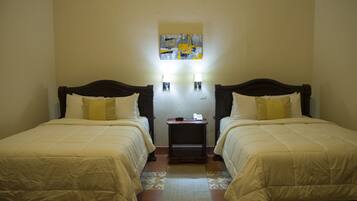 Habitación de hotel con dos camas individuales, una mesita de noche pequeña con un teléfono y dos lámparas de pared.