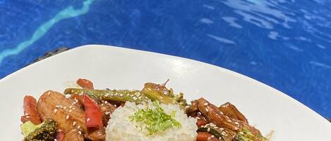 Un plato de verduras y carne salteadas, acompañado de arroz, servido en un plato blanco.