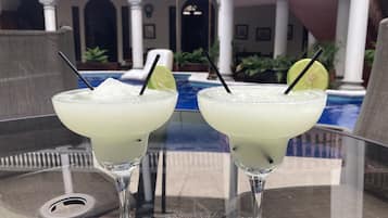 Two margaritas on a glass table with a pool in the background.