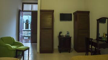 A hotel room with a green armchair, a wooden cabinet with a coffee maker, and a small table with a mirror.