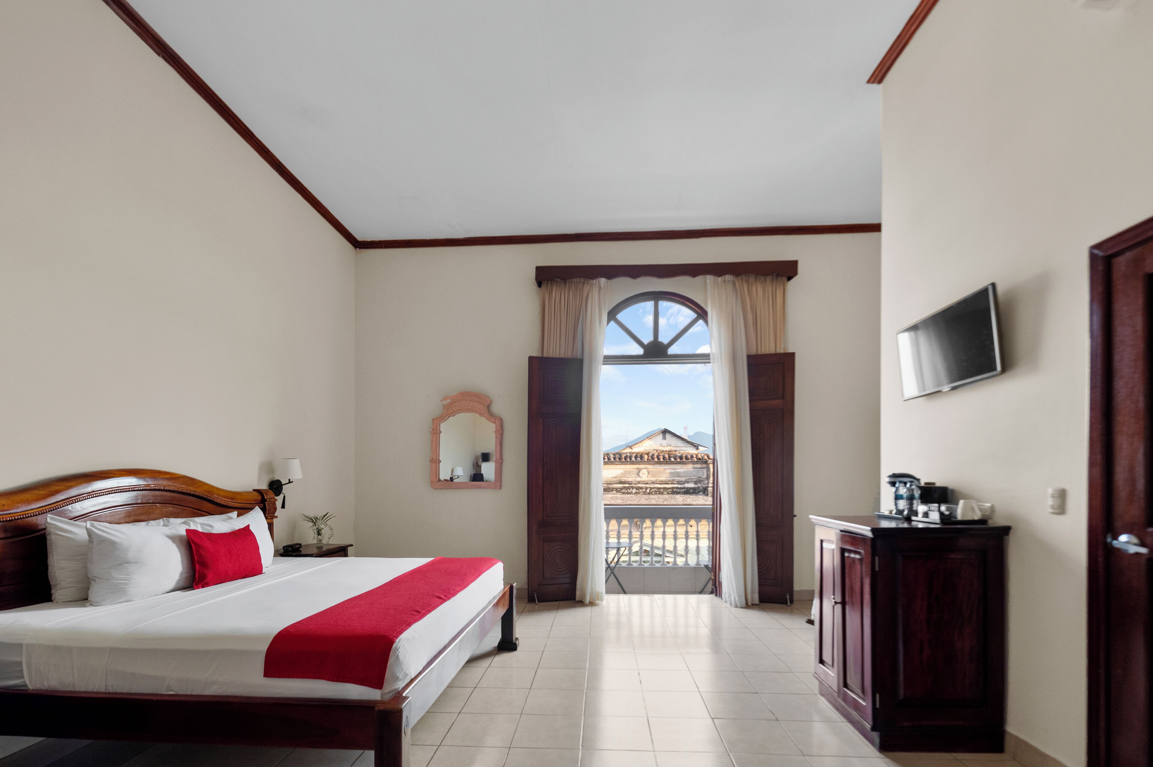 A hotel room with a bed, a TV, a balcony, and a view of a building.