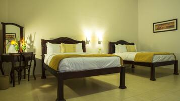 A hotel room with two beds, a desk, a chair, and a lamp.