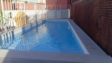 Una piscina al aire libre, sombrillas, sillones reclinables de piscina