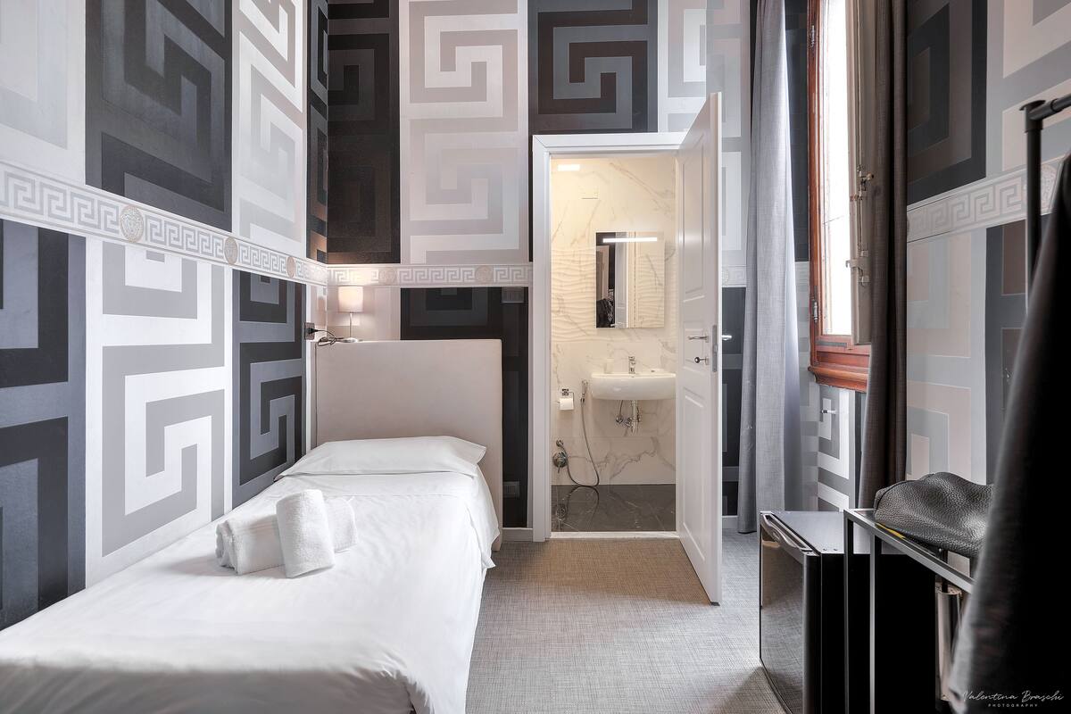 A hotel room with a bed, a bathroom with a sink and mirror, and a door leading to another room.