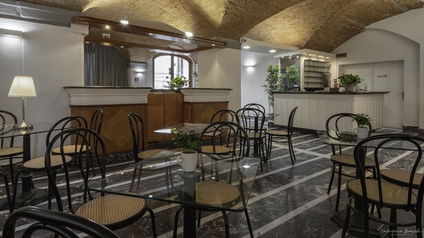 A spacious dining area with high ceilings and exposed brickwork, featuring a central island with a plant, surrounded by black metal chairs and tables. - Hotel Argentina (Florence)