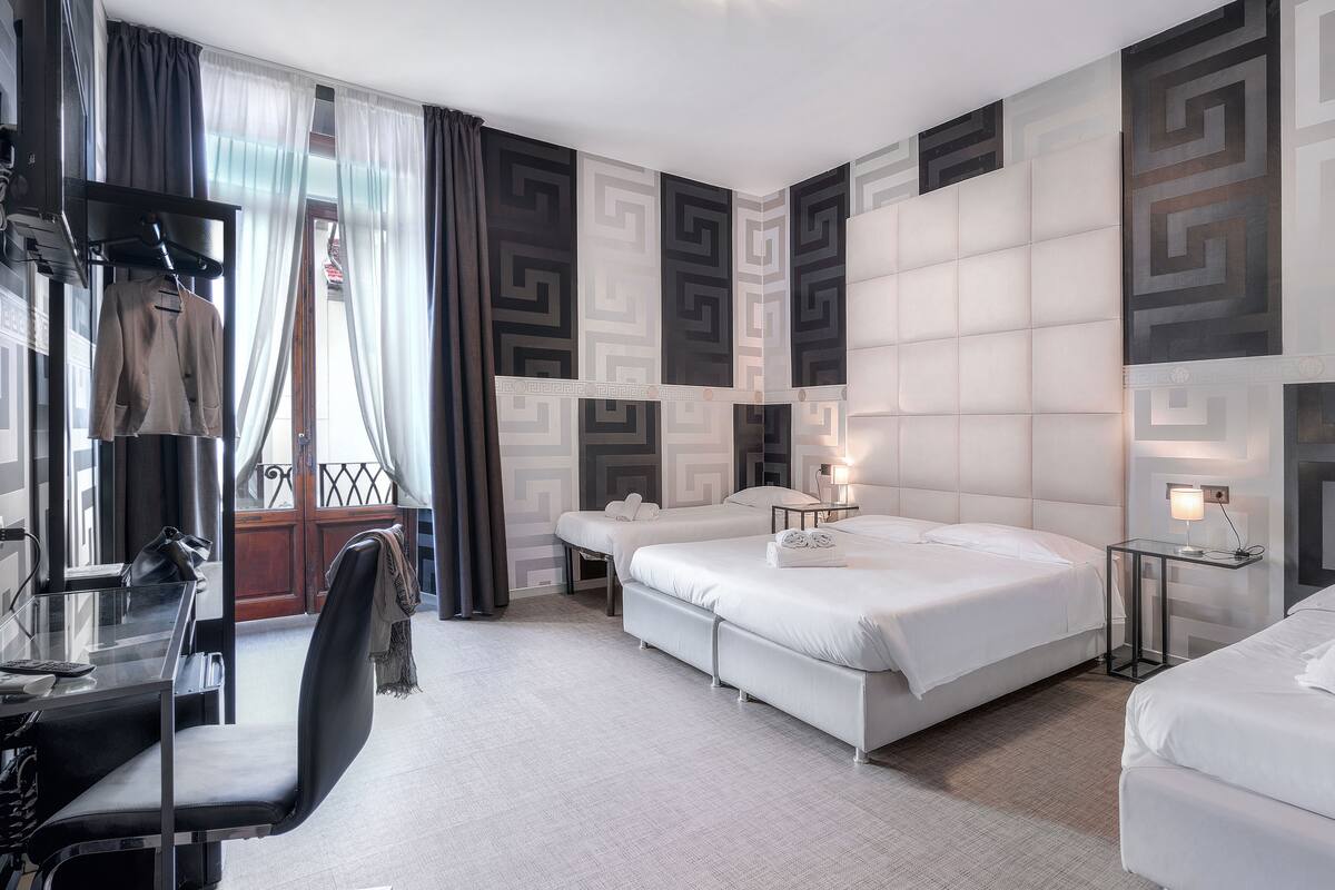 A modern hotel room with a large bed, a desk with a chair, and a small table with a lamp.