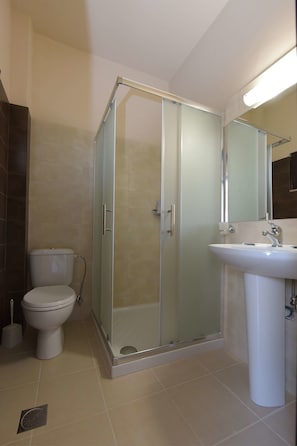 A bathroom with a glass-enclosed shower, a toilet, and a sink with a mirror above it. - Santa Helena Hotel Ialysos (Rhodes)