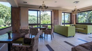 A spacious indoor area with a dining table, chairs, a sofa, and a chandelier. - Santa Helena Hotel Ialysos (Rhodes)