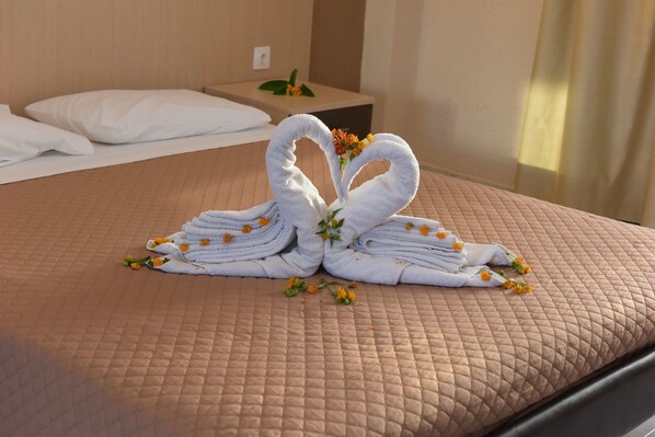 A bed with a quilted bedspread, a neatly made bed with white pillows, and a towel arrangement in the shape of swans with flowers. - Santa Helena Hotel Ialysos (Rhodes)