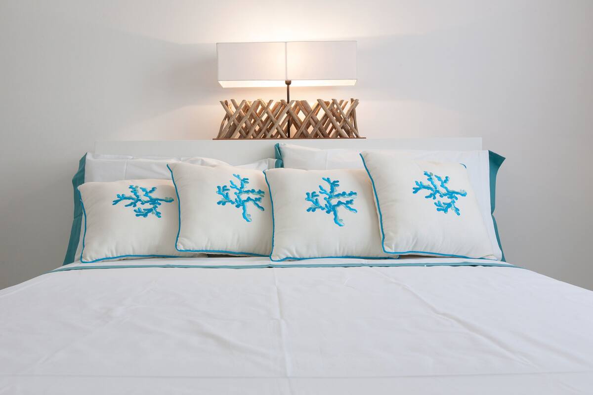 Ein Bett mit weißer Bettwäsche und vier Kissen mit blumigem, blauem Muster.