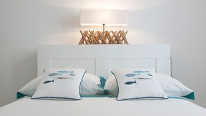 A neatly made bed with two pillows featuring fish designs, a white headboard, and a wall-mounted lamp above. - Le Dimore Turchesi (Salve)