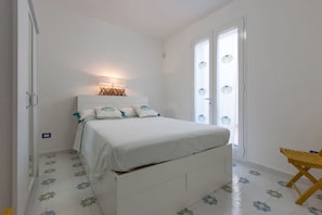 A bedroom with a bed, a bedside table, a lamp, and a window with curtains. - Le Dimore Turchesi (Salve)
