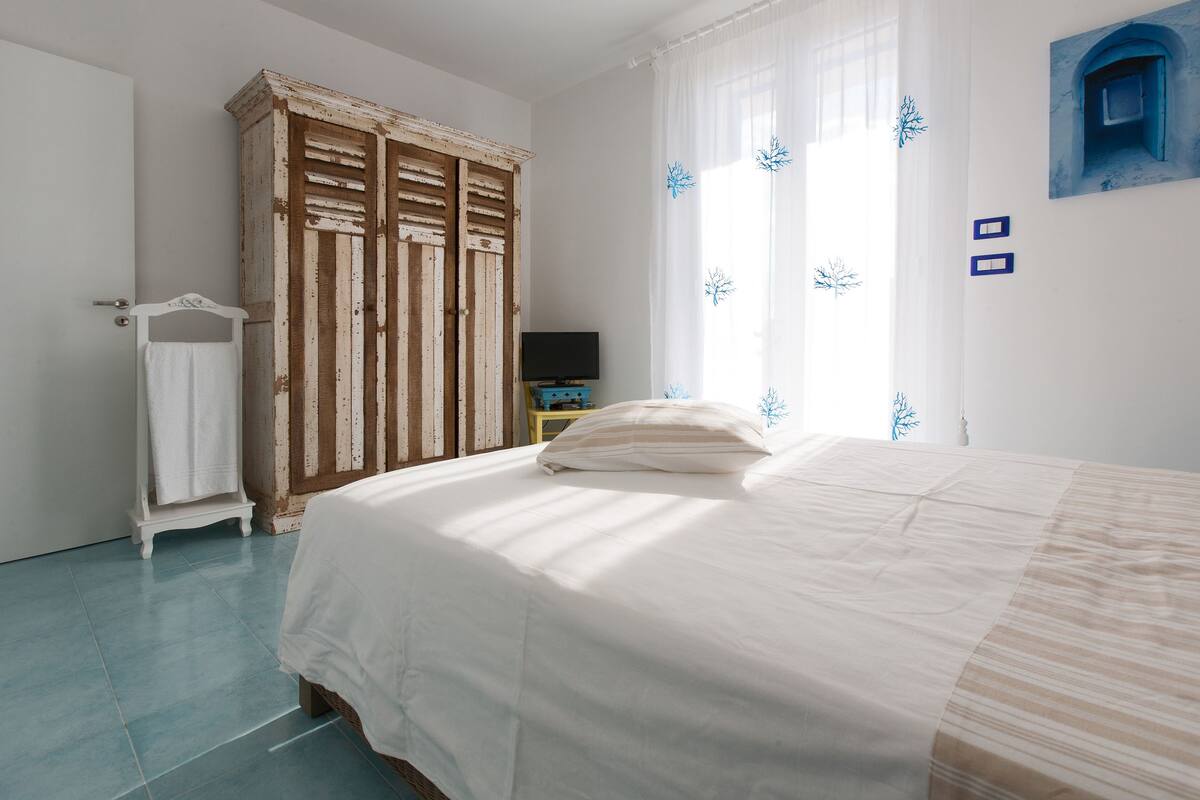 Ein Schlafzimmer mit einem Bett, einem Holzschrank, einem Fernseher auf einem Schrank und einem Fenster mit Vorhängen.