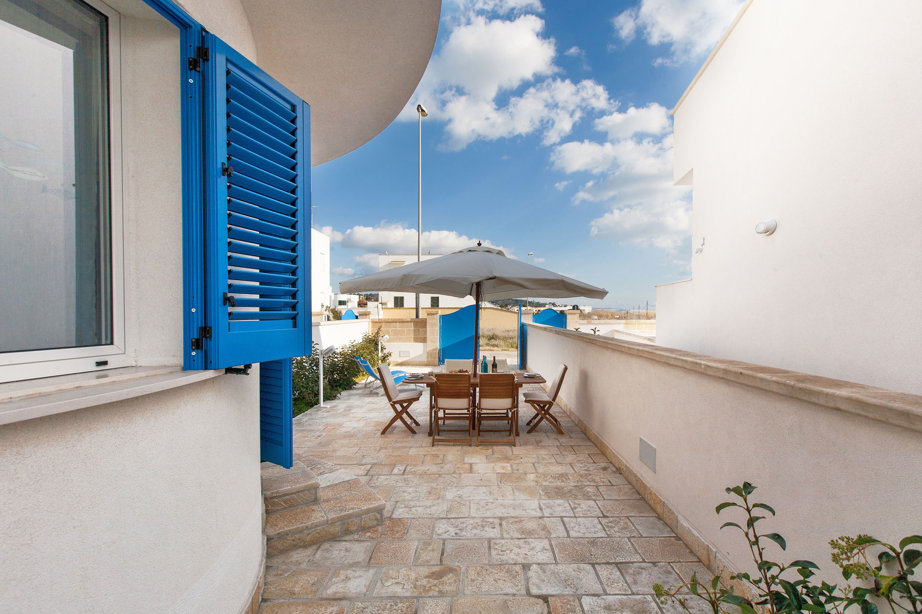 A balcony with a table and chairs, a white umbrella, and a view of the sky.