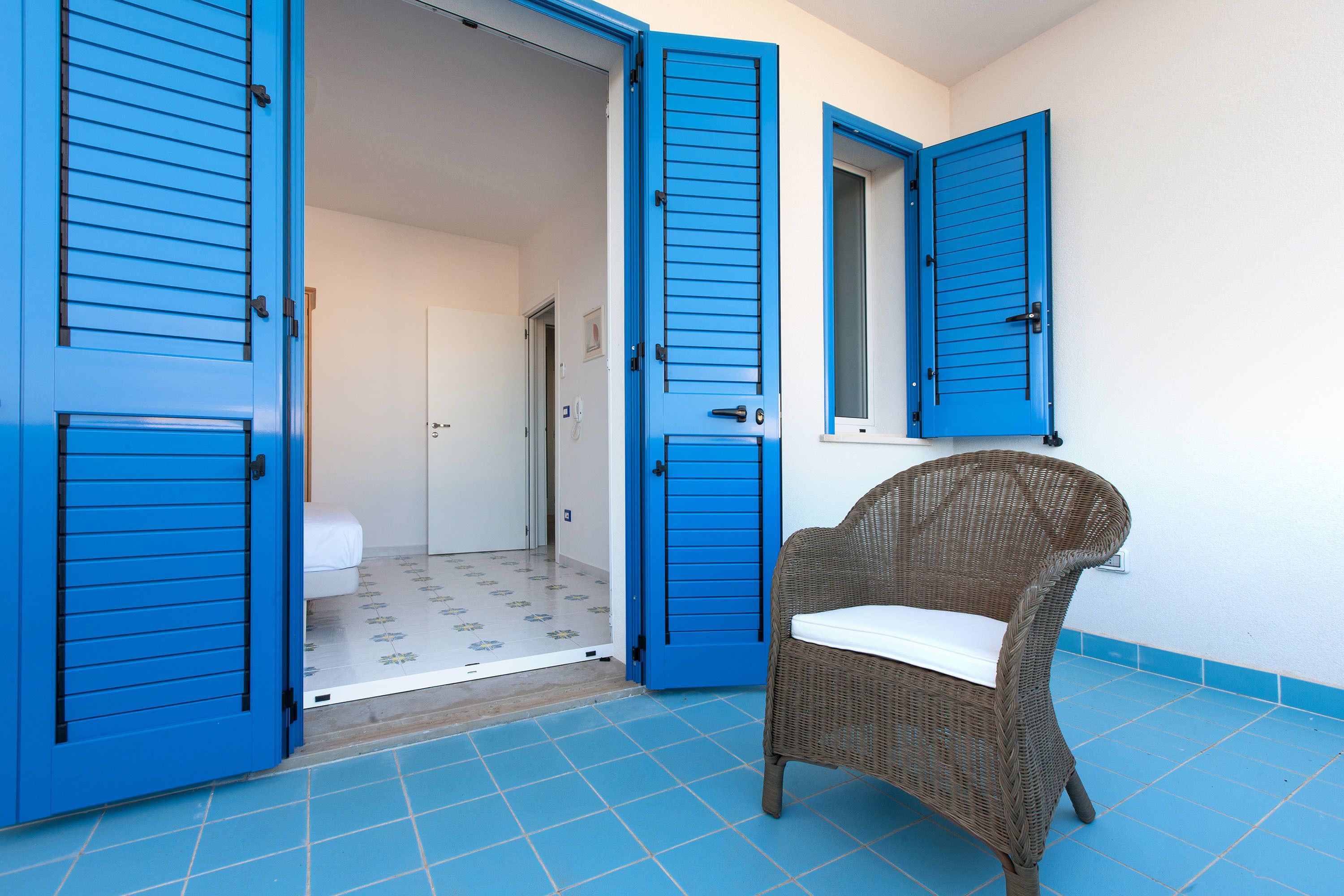 A room with blue shutters, a wicker chair, and a tiled floor.