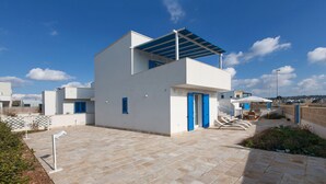 A modern two-story building with a flat roof and blue shutters, featuring a paved courtyard and a view of the surrounding area. - Le Dimore Turchesi (Salve)