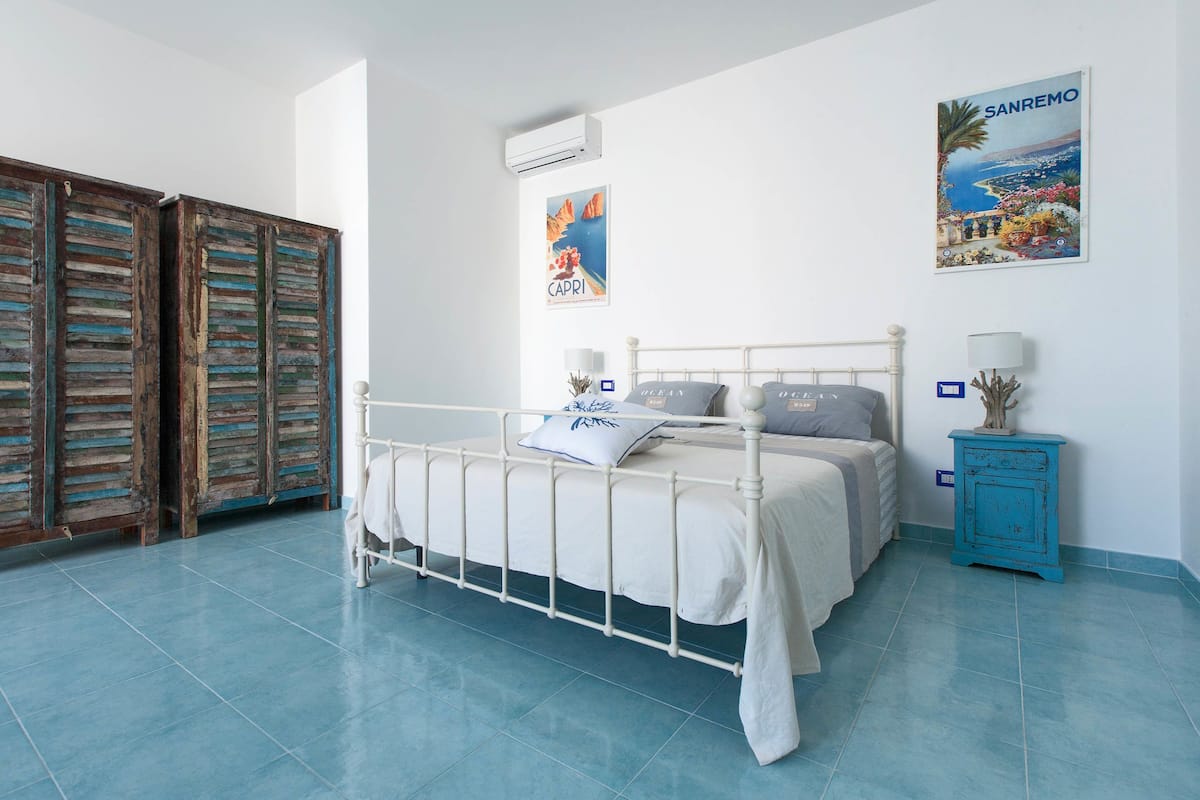 Ein Schlafzimmer mit einem Bett, einem Nachttisch, einem blauen Schrank und einem Bild an der Wand.