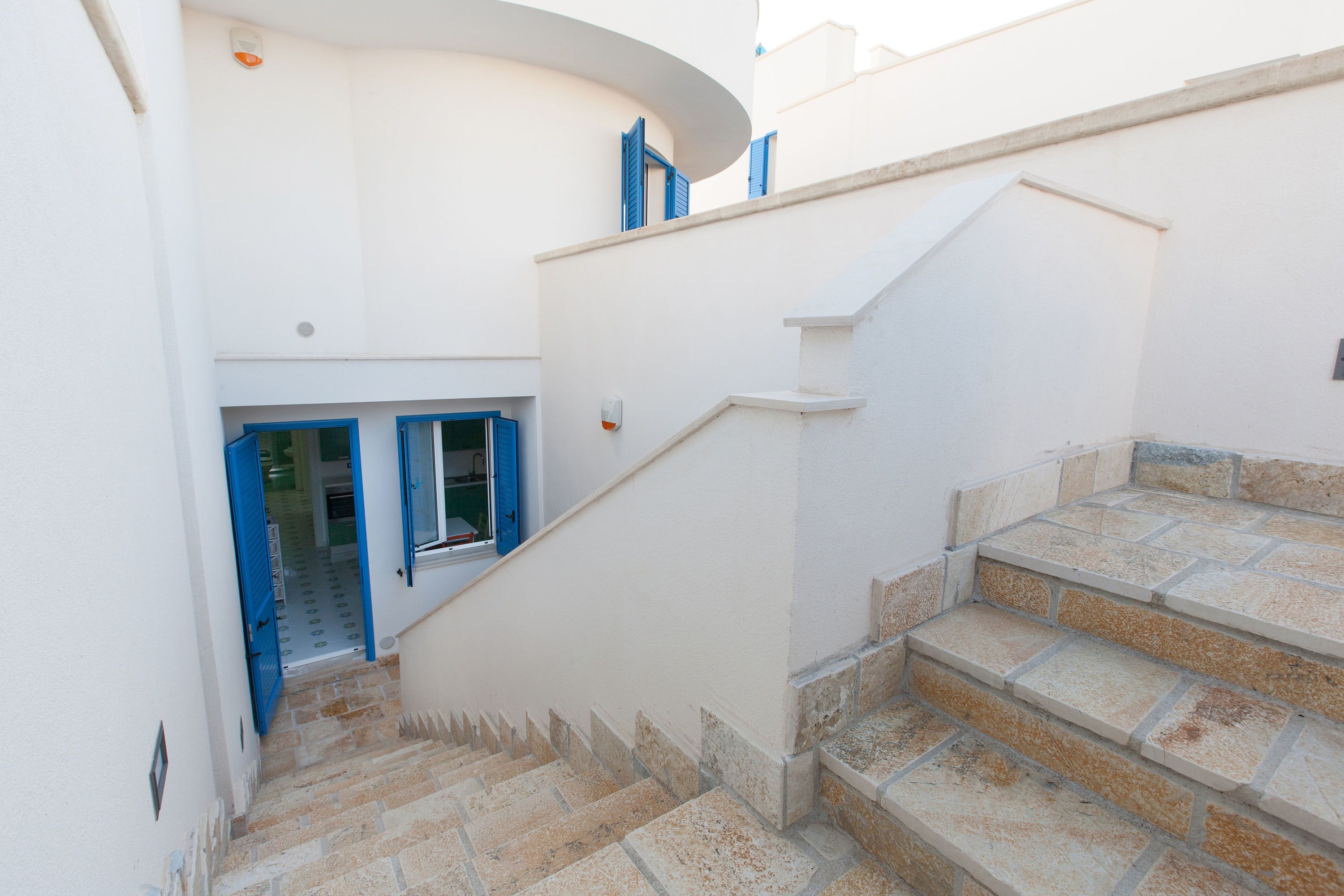 Eine Treppe führt zu einer zweiten Etage mit einer weißen Wand und blauen Fensterläden.