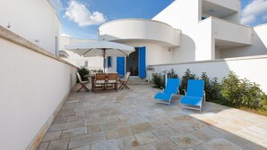 A modern outdoor patio with stone flooring, a dining set, and blue lounge chairs. - Le Dimore Turchesi (Salve)