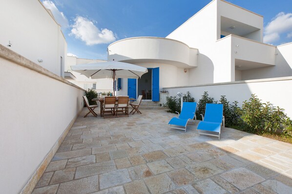 A modern outdoor patio with stone flooring, a dining set, and blue lounge chairs.
